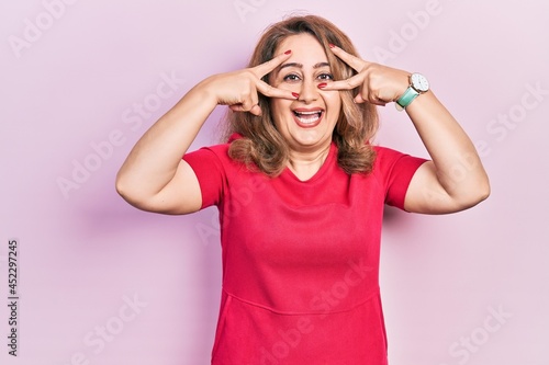 Middle age caucasian woman wearing casual clothes doing peace symbol with fingers over face, smiling cheerful showing victory © Krakenimages.com