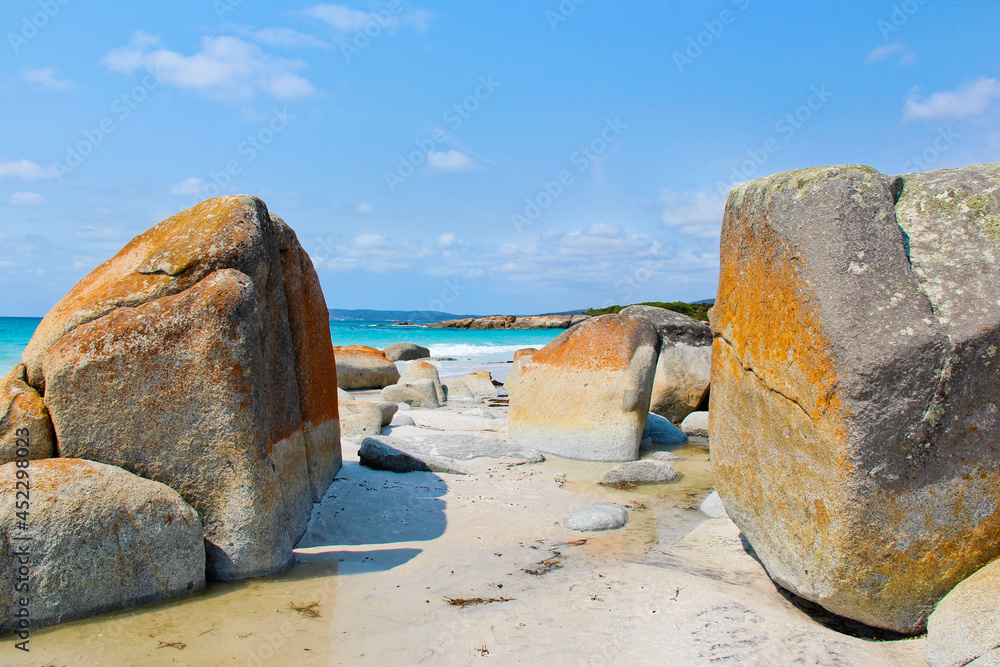 View of turquoise beach between two large rocks covered in orange lichen. Bay of Fires. No people, space for copy.