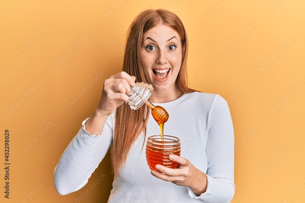 Young irish woman holding honey celebrating crazy and amazed for success with open eyes screaming excited. Young irish woman holding honey celebrating crazy and amazed for success with open eyes screaming excited.