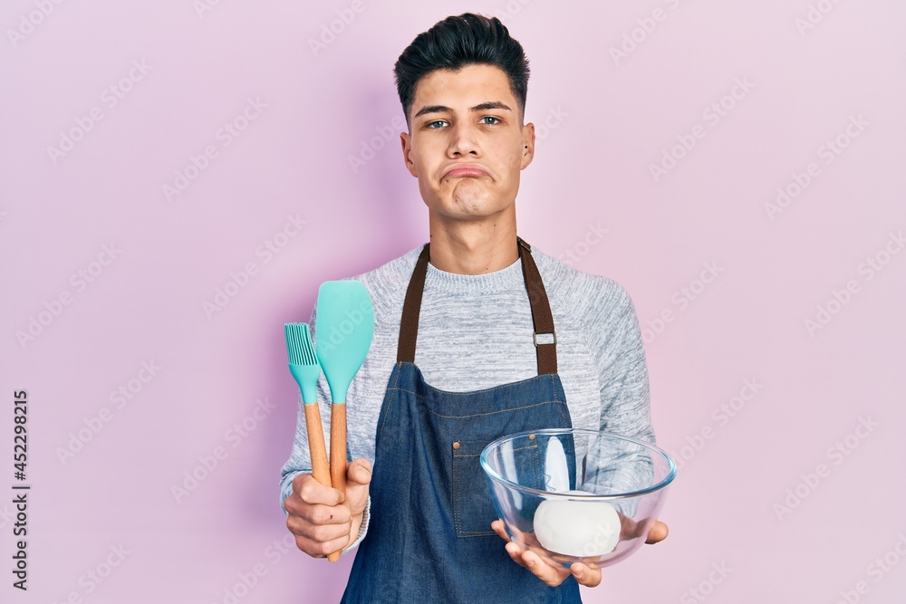 Young hispanic man holding bread dough and cooking tools depressed and worry for distress, crying angry and afraid. sad expression. Young hispanic man holding bread dough and cooking tools depressed and worry for distress, crying angry and afraid. sad expression.