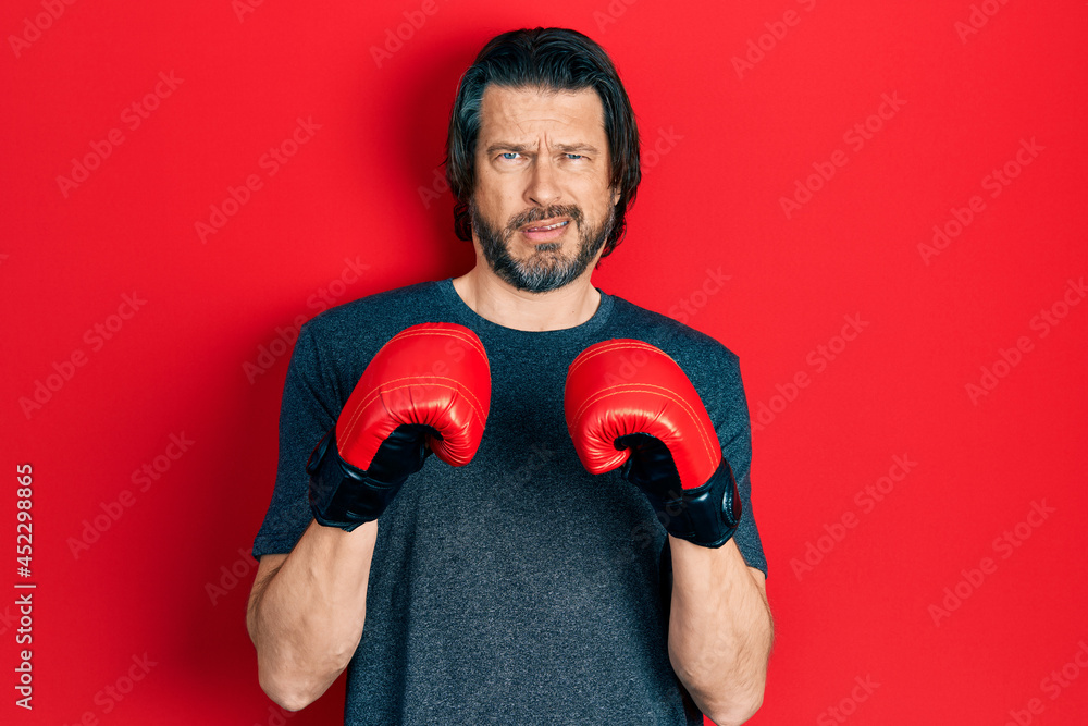 Middle age caucasian man using boxing gloves clueless and confused expression. doubt concept.