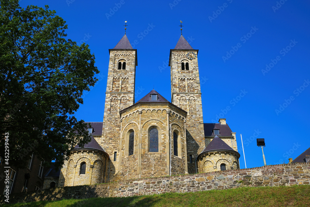View on roman basilica and monastery from 11th century with two towers on green hill against blue summer sky - Sint Odilienberg, Netherlands