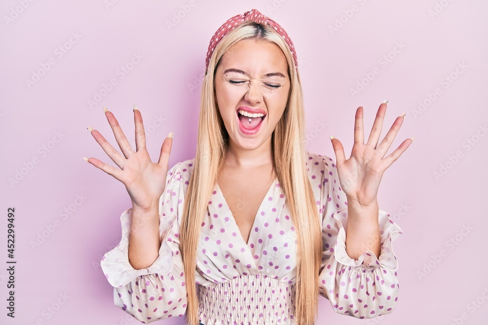 Young blonde girl wearing casual clothes celebrating mad and crazy for success with arms raised and closed eyes screaming excited. winner concept Young blonde girl wearing casual clothes celebrating mad and crazy for success with arms raised and closed eyes screaming excited. winner concept