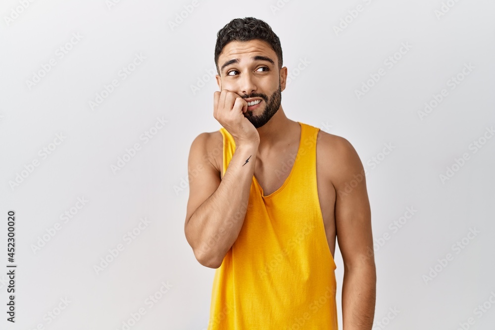 Young handsome man with beard standing over isolated background looking stressed and nervous with hands on mouth biting nails. anxiety problem.