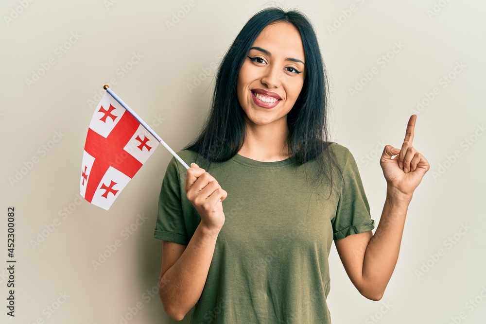 Young hispanic girl holding georgia flag smiling happy pointing with hand and finger to the side Young hispanic girl holding georgia flag smiling happy pointing with hand and finger to the side