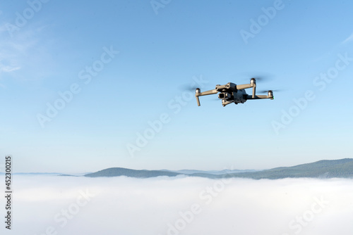 flying a quadrocopter helicopter drone in the air, in a clear blue sky, morning fog and mountains below. aerial photo and video shooting using gadgets and modern devices. modern technologies allow you