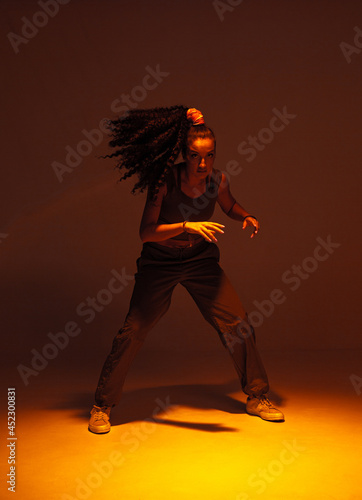 Dancing mixed race girl inshadow in studio. Female dancer performer moving in expressive ethnic hip hop dance photo