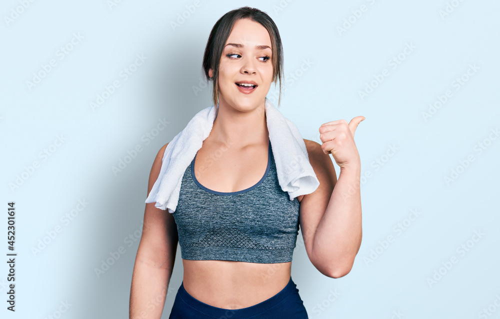 Young hispanic girl wearing sportswear and towel smiling with happy face looking and pointing to the side with thumb up. Young hispanic girl wearing sportswear and towel smiling with happy face looking and pointing to the side with thumb up.