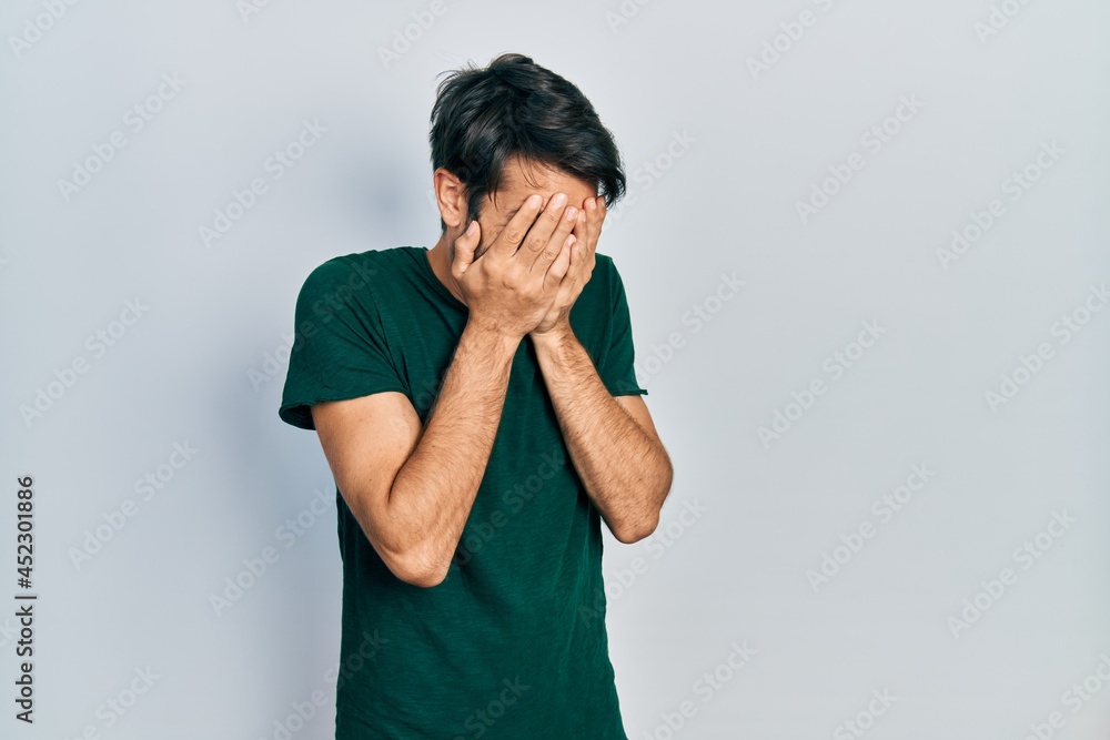Young hispanic man wearing casual white tshirt with sad expression covering face with hands while crying. depression concept. Young hispanic man wearing casual white tshirt with sad expression covering face with hands while crying. depression concept.
