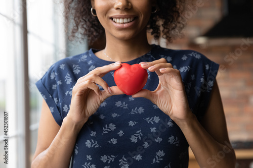 Happy African American volunteer girl holding red heart, showing object at camera, smiling. Black young woman promoting charity, donation campaign, health insurance, medical checkup. Close up of hands