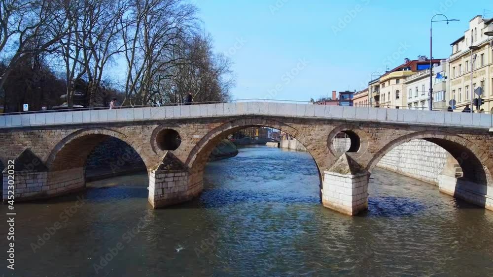 Drone with camera flying over the river Miljacka under old pedestrian Latin bridge, where heir to the throne of Austria-Hungary Franz Ferdinand was killed, Bosnia and Herzegovina. Drone with camera flying over the river Miljacka under old pedestrian Latin bridge, where heir to the throne of Austria-Hungary Franz Ferdinand was killed, Bosnia and Herzegovina.