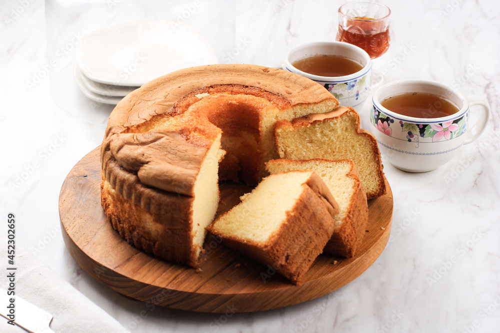 Slice of Fluffly Vanilla Chiffon Cake or Sponge Cake on Wooden Plate, Served with Tea and Honey. Bright Food Photography Concept for Bakery. Selected Focus Slice of Fluffly Vanilla Chiffon Cake or Sponge Cake on Wooden Plate, Served with Tea and Honey. Bright Food Photography Concept for Bakery. Selected Focus