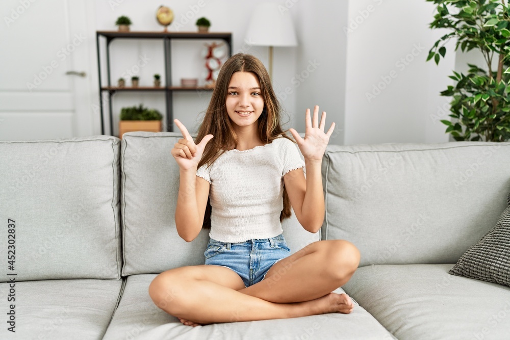 Young brunette teenager sitting on the sofa at home showing and pointing up with fingers number seven while smiling confident and happy. Young brunette teenager sitting on the sofa at home showing and pointing up with fingers number seven while smiling confident and happy.