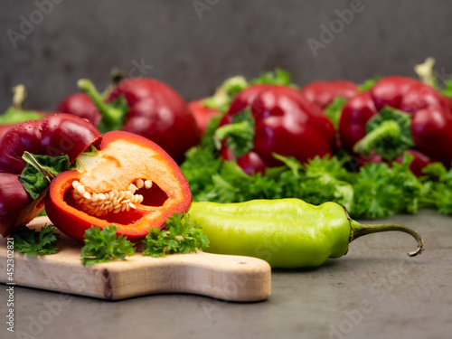 Red, bell peppers, chopped in half, and parsley on a wooden cutting board. Gray background. Vegetables.