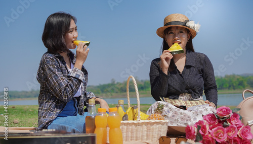 two young asian women eating watermelon while vacationing by the lake