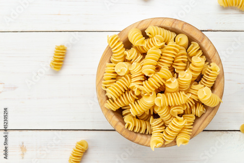 Raw Pasta Fusilli in Wooden Bowl on White Rustic Background.
