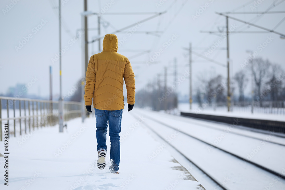 Rear view of loneliness person in warm clothing. Man leaves train station against snowy landscape..