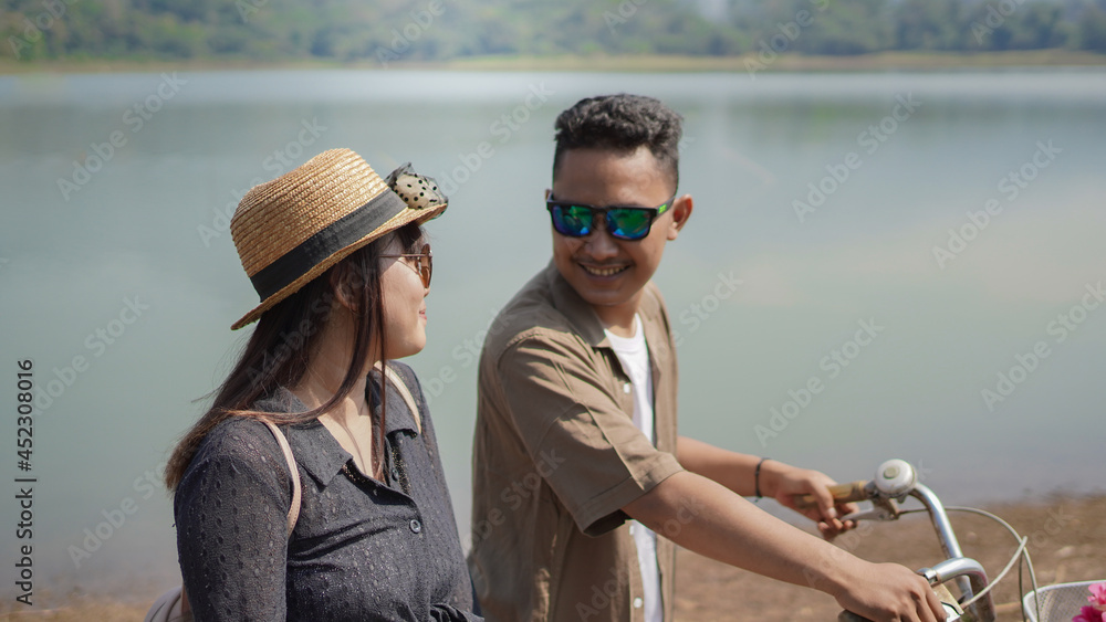 happy young asian couple walking bicycle in park in summer