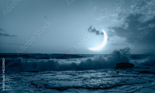 Waves crashing over rocks from the ocean with amazing crescent moon