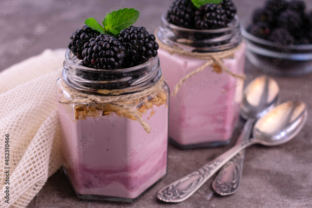 Yogurt with blackberries in jars on a gray background.
Close-up. Yogurt with blackberries in jars on a gray background.
Close-up.