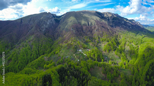 Aerial drone view above Buila Vanturarita Massif and Patrunsa Monastery - a rural settlement located on the hills at the base of the mountain.
