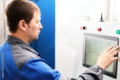 Portrait of an employee in overalls at work at an industrial facility. A man at the monitor of production equipment checks the readings and monitors the system. A real worker.