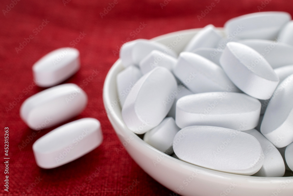 Several vitamin tablets in a white ceramic saucer on a red linen napkin, close-up. Several vitamin tablets in a white ceramic saucer on a red linen napkin, close-up.