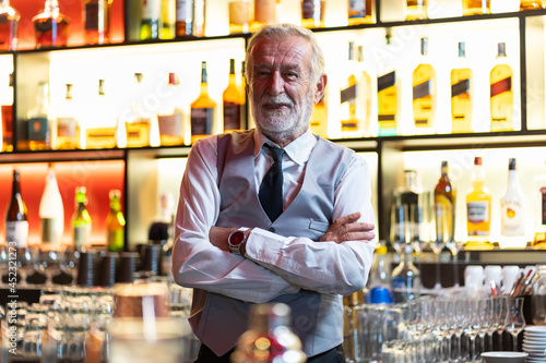 Smiling senior barman or waiter in apron on wine or alcohol blur background. Senior bartender smiling with arms crossed at the bar. alcohol, people, service concept