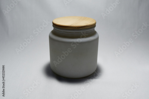 White ceramic jar with wooden lid on white background candle inside