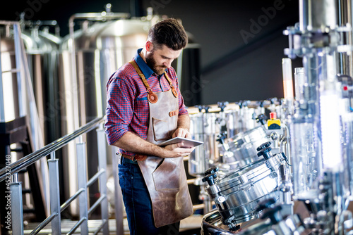 Young male brewer in leather apron supervising the process of beer fermentation at modern brewery factory © romaset