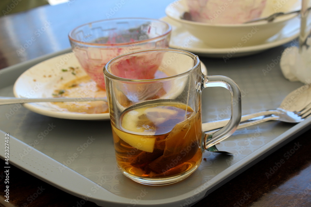 There are dirty dishes and unfinished tea on the tray. There are dirty dishes and unfinished tea on the tray.
