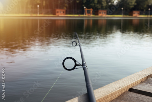Fishing rod laying on wooden coast over river or lake in summer.