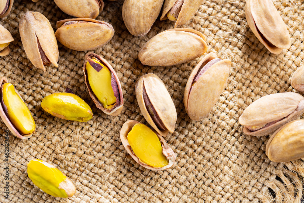 Naklejka premium Pistachios nuts on a burlap. Salted, roasted green pistachios on sackcloth background. Healthy snack. Top view