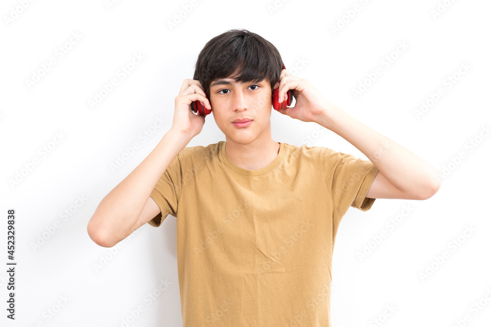 A teenager boy with wireless headphones on his head listens to music on a white background. A teenager boy with wireless headphones on his head listens to music on a white background.