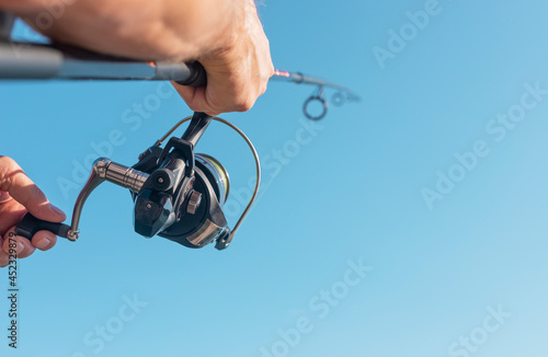 Men hands holding flying fishing rod or angler over blue clear sky.