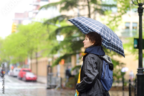 Foto Mature woman tourist with umbrella walking on street of Manhattan in cool rainy spring day