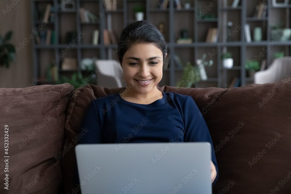 Smiling mixed race female look at laptop screen work online at home office on weekend. Happy Indian woman use modern computer gadget browse wireless internet or talk on video call on web. Smiling mixed race female look at laptop screen work online at home office on weekend. Happy Indian woman use modern computer gadget browse wireless internet or talk on video call on web.