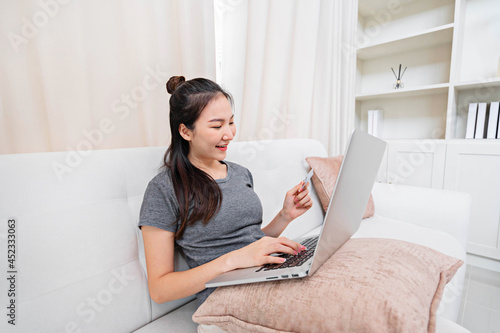 Asian woman using credit card for online payment with laptop while sitting at the living room. online shopping Pay by credit card via electronic wallet.