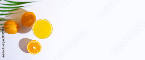 glass with fresh juice, oranges and a leaf of a palm tree on a light background. Top view, flat lay. Banner
