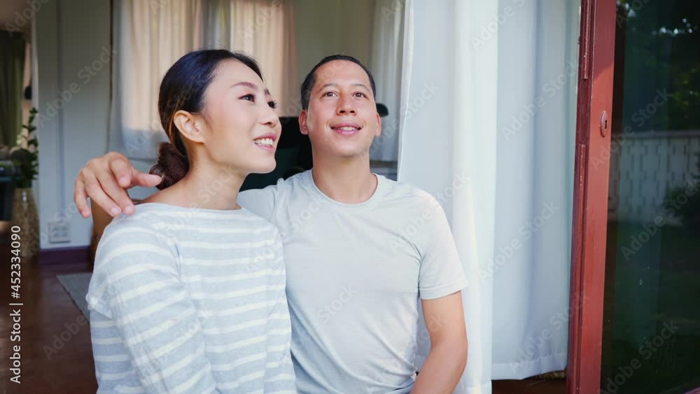 Portrait of young adult Asian couple looking up while a man is pointing with a finger in home interior background. 30s mature successful husband and wife - 4K Slow Motion Footage Portrait of young adult Asian couple looking up while a man is pointing with a finger in home interior background. 30s mature successful husband and wife - 4K Slow Motion Footage