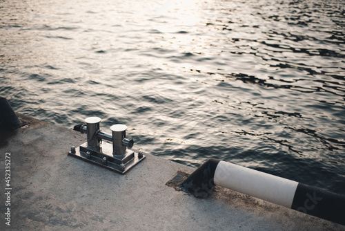 Metal bollard for boats and vessels on wharf over sea and sunset background close up. Maritime quayside with equipment for yatching at coastline. Travel season. photo