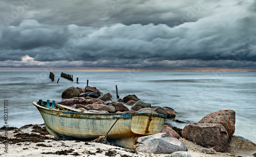 Coastal landscape with broken abandoned  pier and beached old fishing boat af...