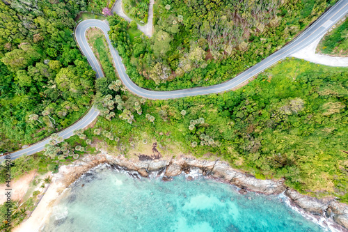 Aerial drone top down view of waves breaking in the sand with road and forest. High angle view of tropical sea with Seafront road.