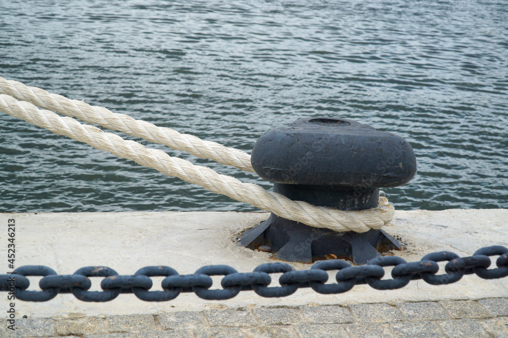 Bollard with a rope on the background of the ship's chain and sea water.