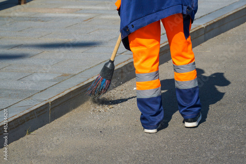 A janitor in a bright special uniform with reflective stripes sweeps the street with a broom.