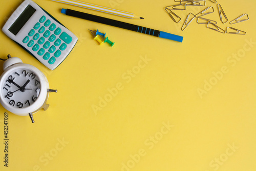 Alarm clock, calculator and stationery on a yellow background, copy space