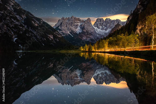 il monte cristallo visto dal lago di landro in notturna, con il bosco illuminato dai fari delle auto di passaggio, sotto un cielo stellato photo