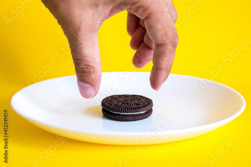 cookies on a white plate on a yellow background. The hand reaches for the cookie. Chocolate cookies with sweet cream are a very popular dessert in Russia.