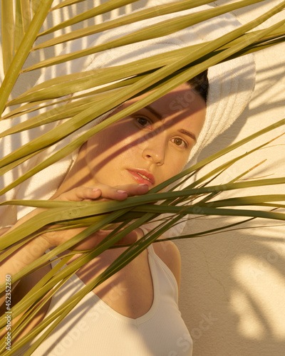 woman with white towel on head ans in white top posing with palm leaf and shadow