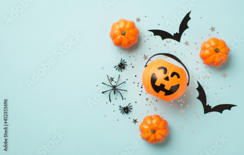 Top view photo of halloween decorations pumpkin basket silver sequins stars spiders and bat silhouettes on isolated pastel blue background with copyspace photo